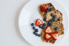 Brown pancakes from whole grain oats served with fresh bluberry and sliced strawberry on white background. Healthy dessert